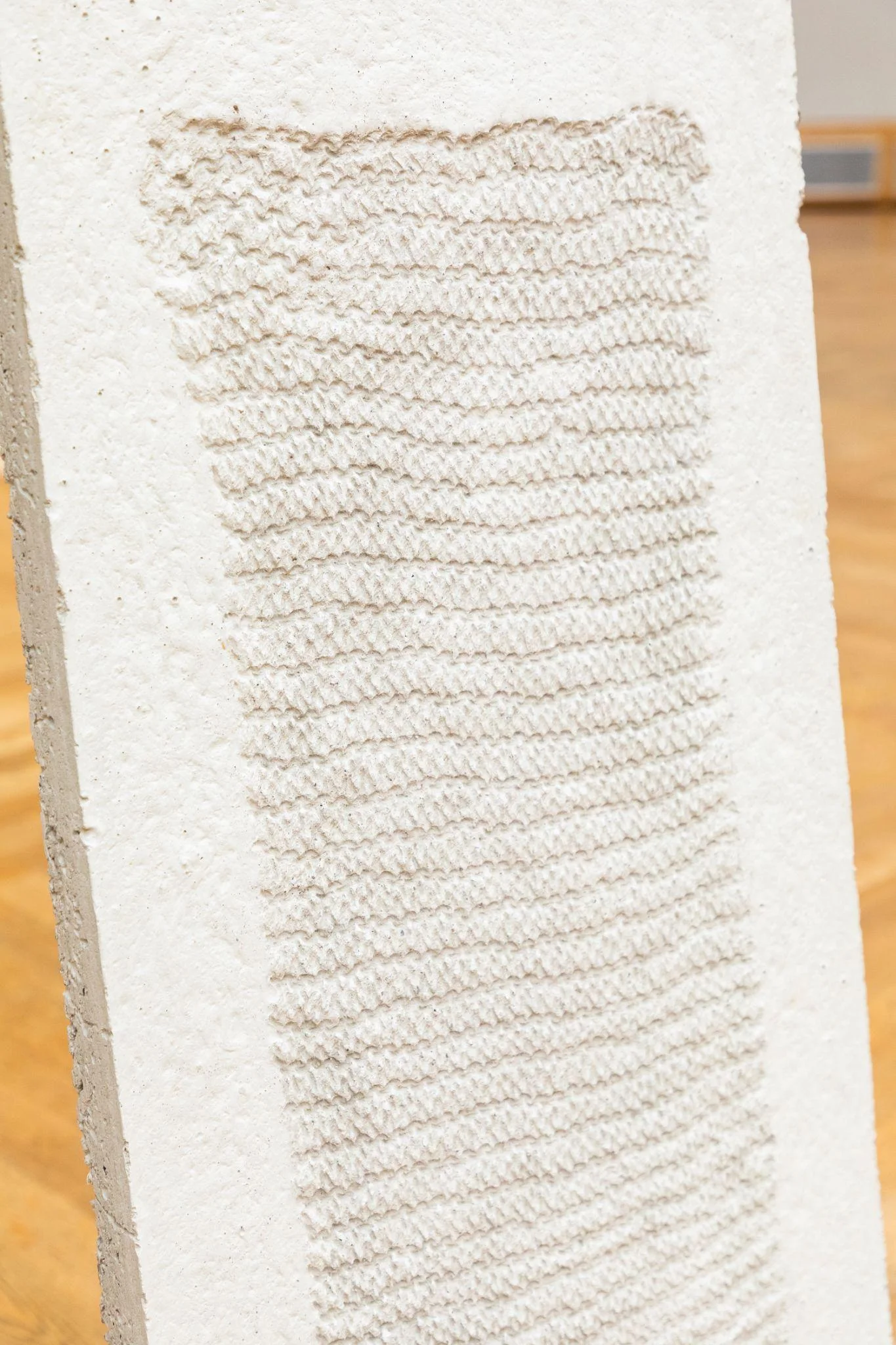 White sculptural panel bearing an impression of textile stitches